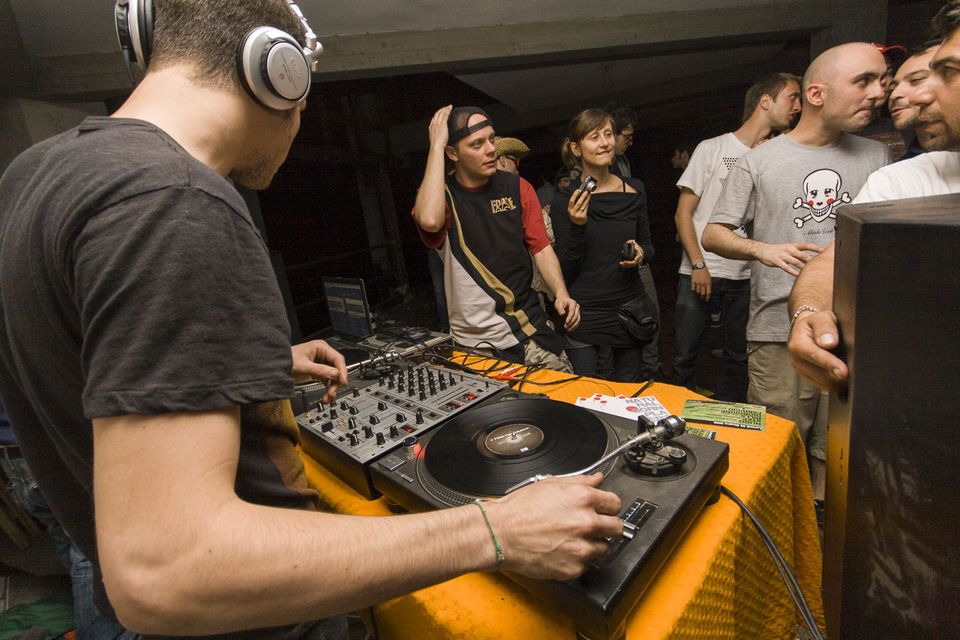 DJ in headphones mixing on turntables with a crowd behind
