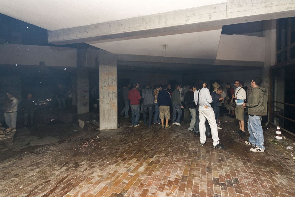 Guests standing in a dim concrete hall with a brick-paved floor