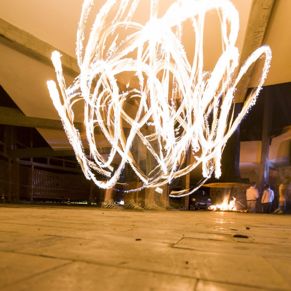Long-exposure fire trails above a paved floor and a distant bonfire
