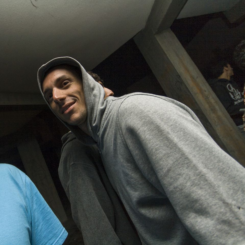 Smiling man in a grey hoodie leaning toward the camera