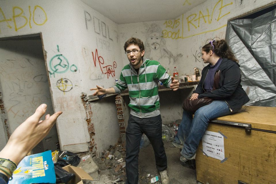Partygoers chatting beside a graffiti-covered wall and a wooden crate