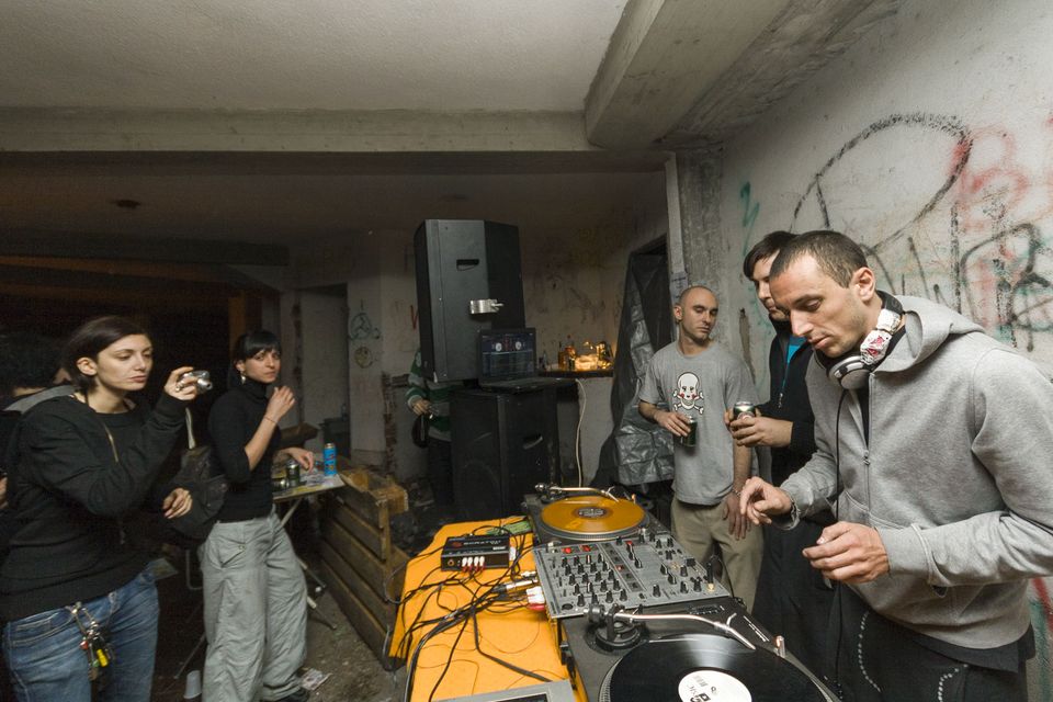 DJ at the decks beside a graffiti wall as guests take photos
