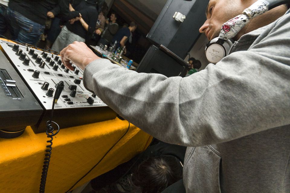Close-up of a mixer’s knobs and faders with a DJ in headphones
