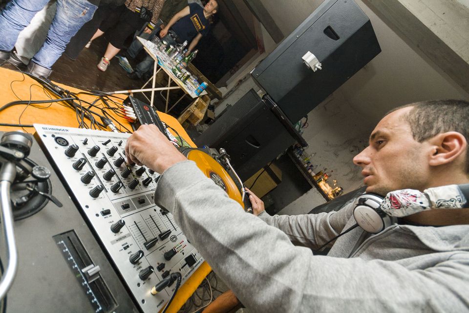 DJ concentrating over the mixer and turntable in a bare room