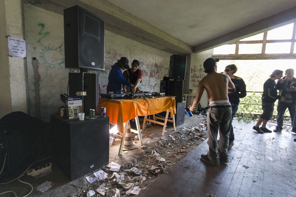 DJ table and speakers under a concrete roof above a littered floor