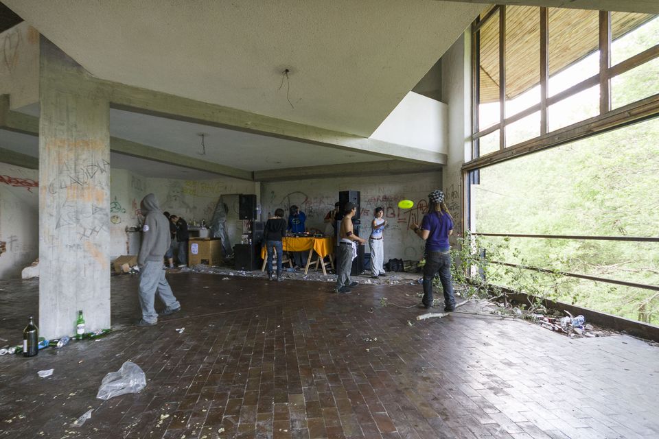Concrete hall opening onto forest with a DJ table in the distance