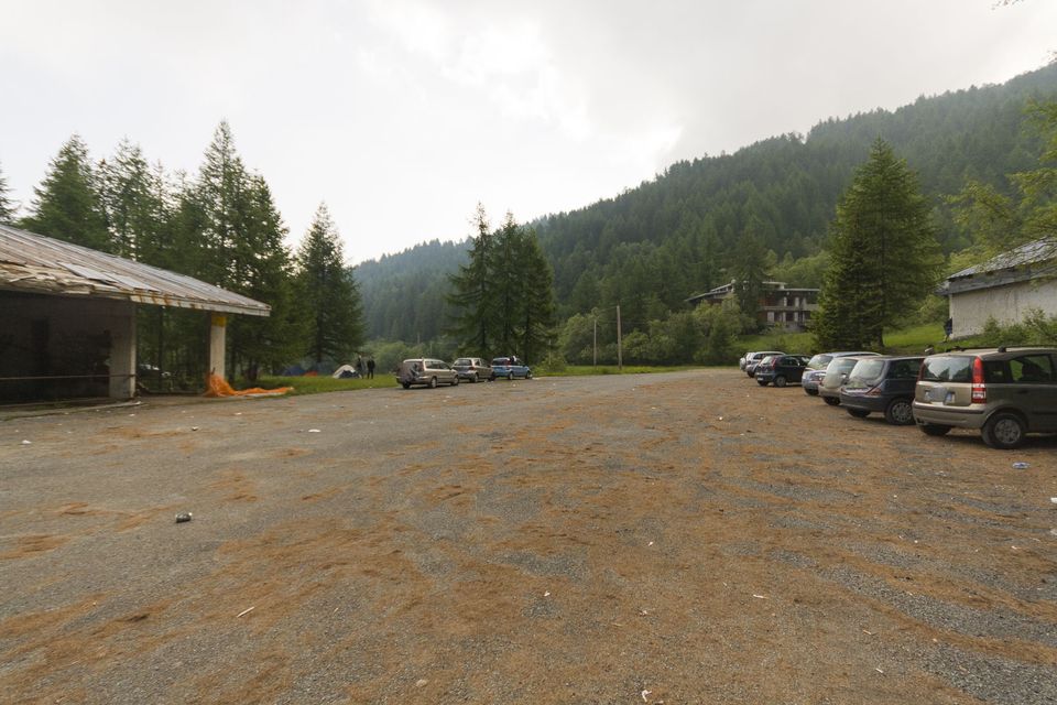 Gravel car park with parked cars below conifer-covered mountain slopes
