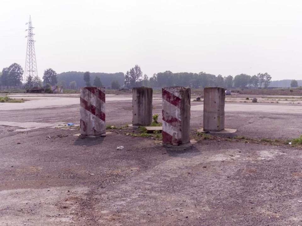 Red-and-white striped concrete posts on a cleared factory site with a pylon