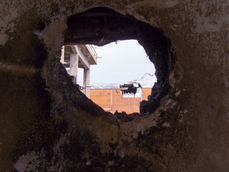 Rough hole in a blackened wall framing a brick building and sky