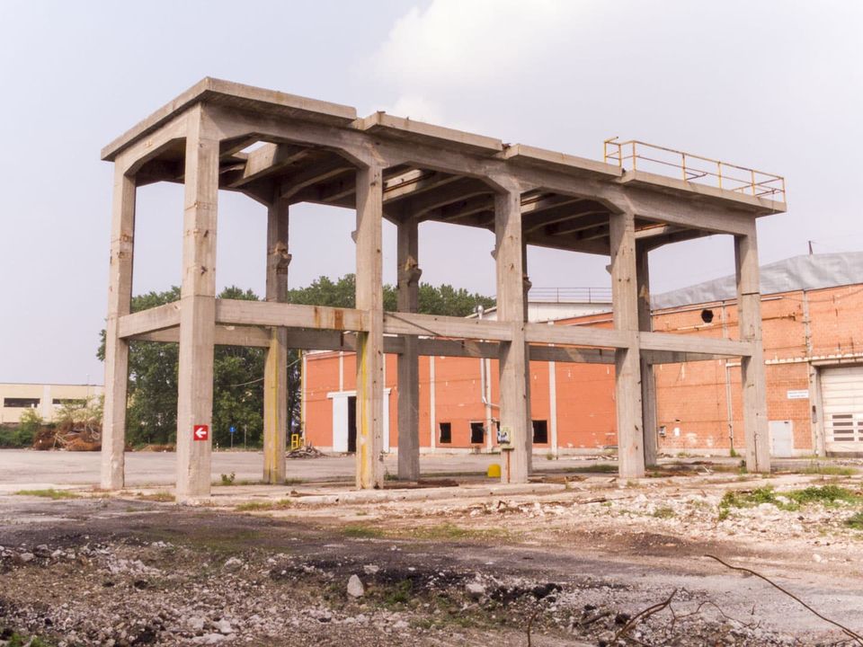 Concrete frame structure on a cleared site beside an orange brick hall