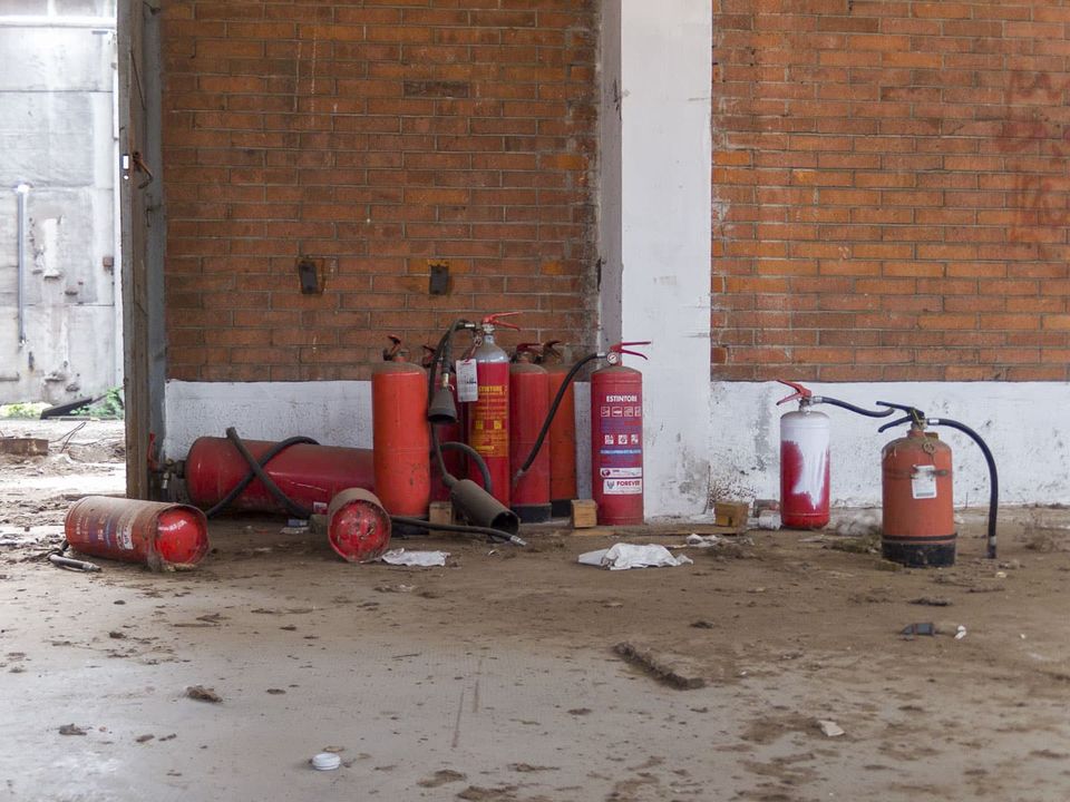 Discarded red fire extinguishers against a brick wall in an empty hall