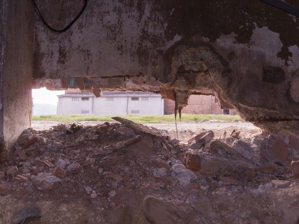 Gap in a wall above rubble, looking out to a field