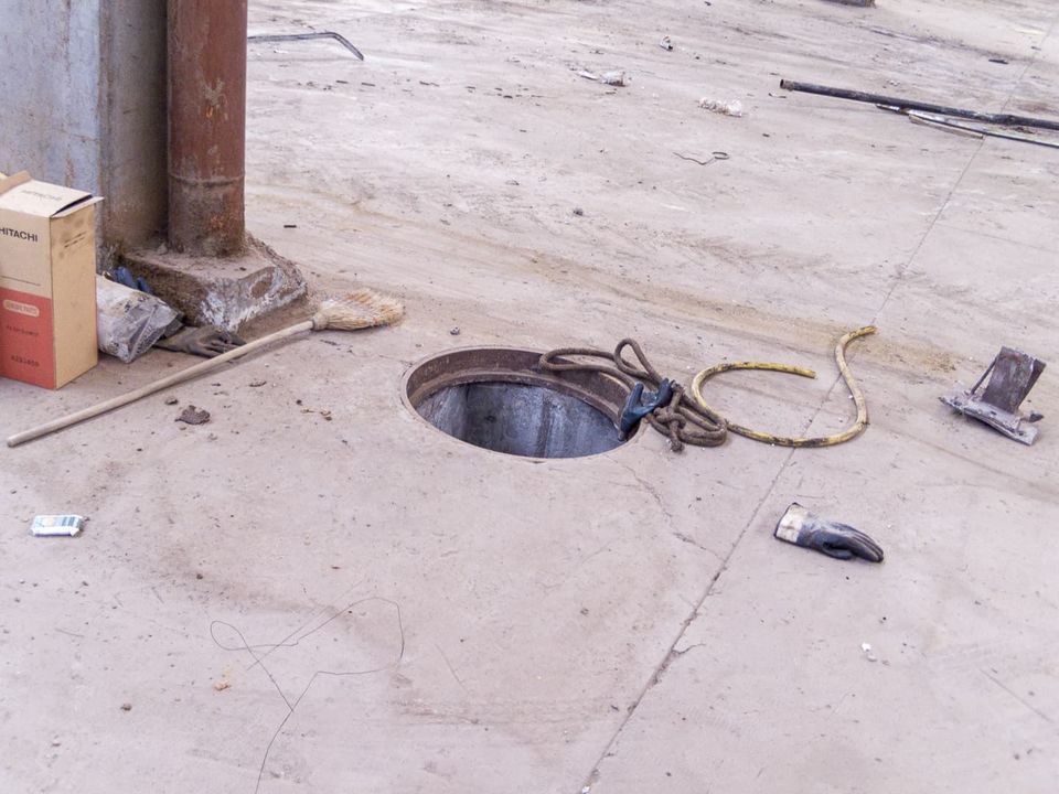 Open manhole with rope and a broom on a dusty concrete floor
