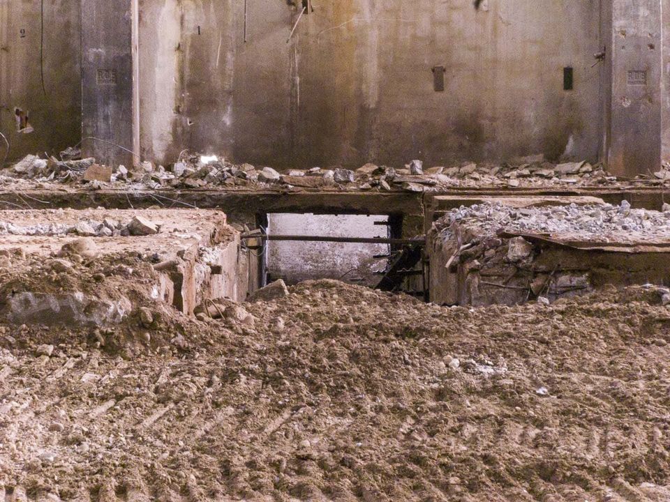 Rubble mounds in a gutted hall with tyre tracks in the dirt