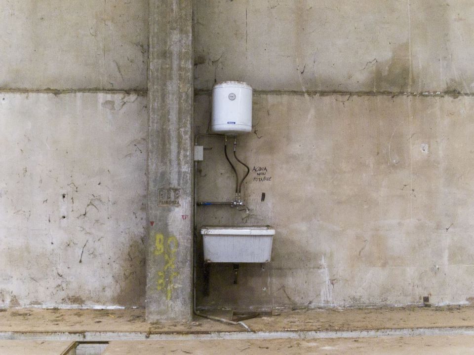 Water heater and small sink bolted to a bare concrete wall
