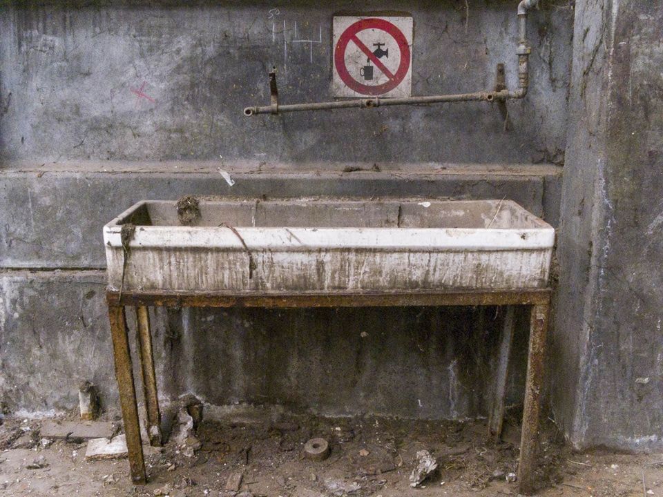 Old stained basin on rusty legs below a no-water sign
