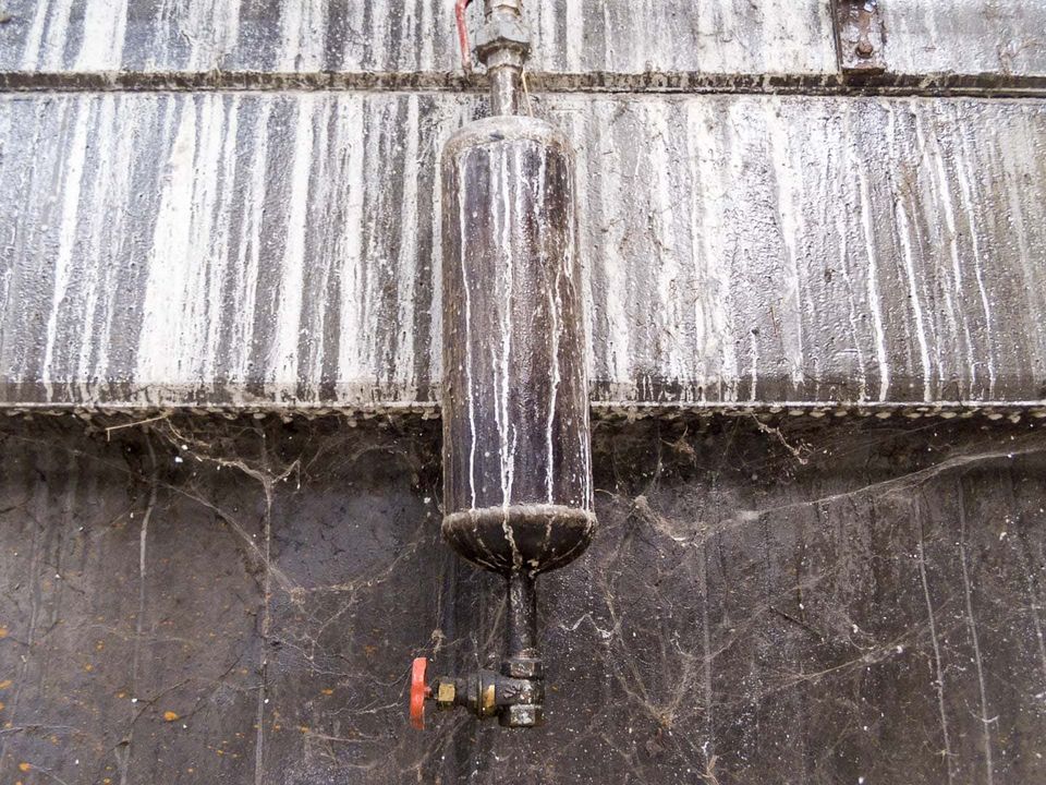 Cobwebbed pressure vessel with a red valve on a stained wall
