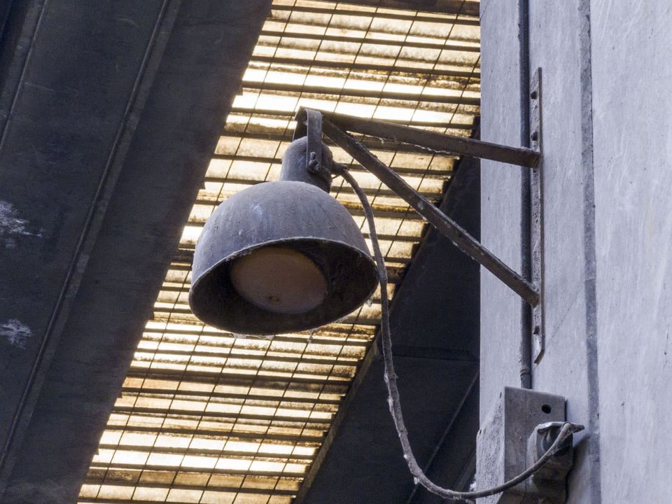 Rusty floodlight bracketed to a wall under a translucent roof