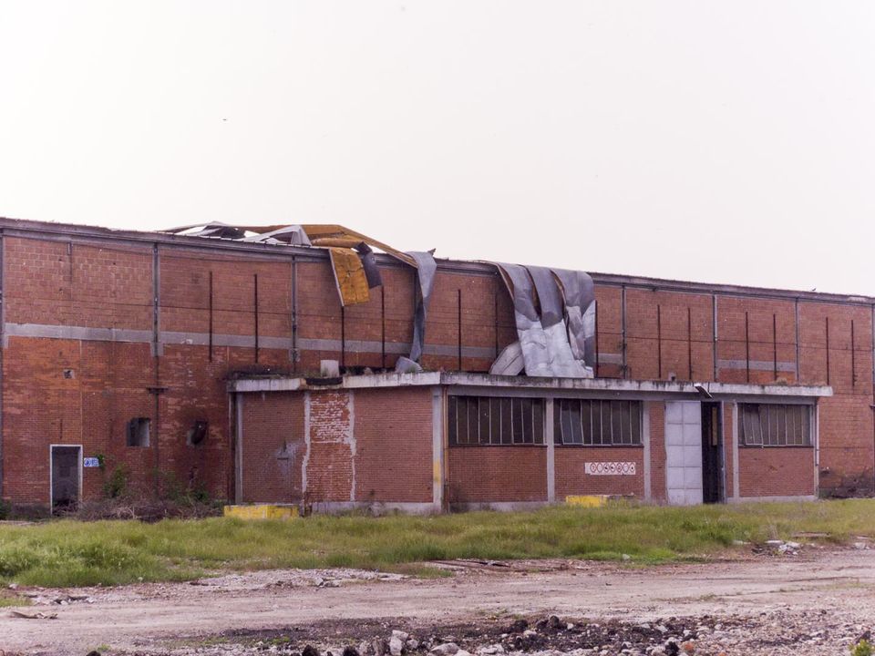 Brick factory hall with torn roof sheeting hanging over the edge
