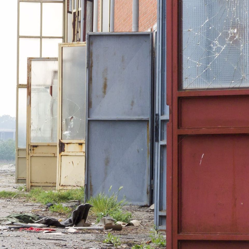 Row of old metal doors and cracked glass panels in the weeds