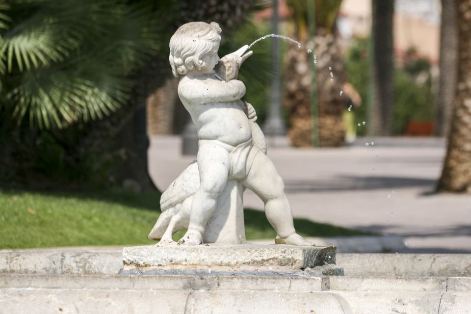 White marble cherub fountain spouting water among palms