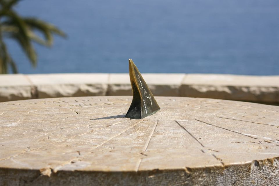 Bronze sundial gnomon on a stone disc above the blue sea