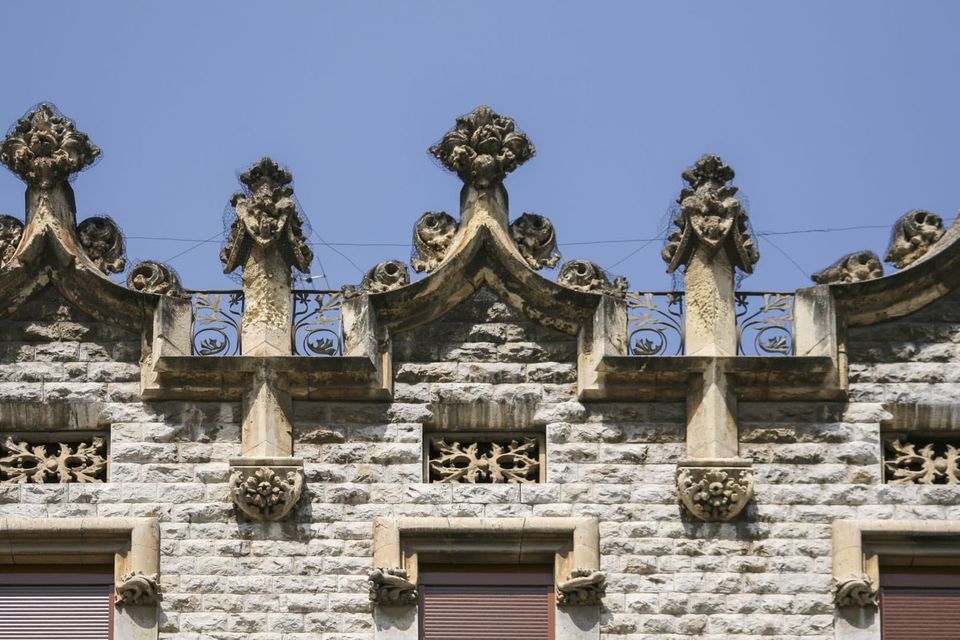 Carved stone finials along a roofline above shuttered windows