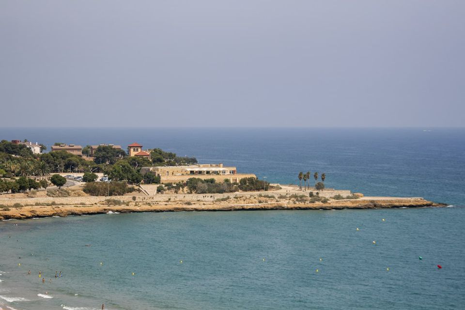 Rocky headland with a low building and palms above turquoise water