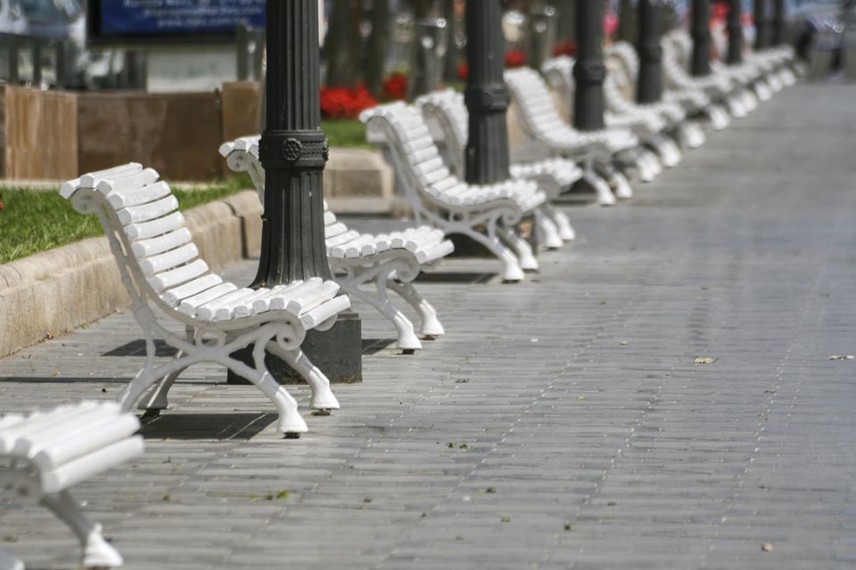 Row of white park benches along a paved promenade
