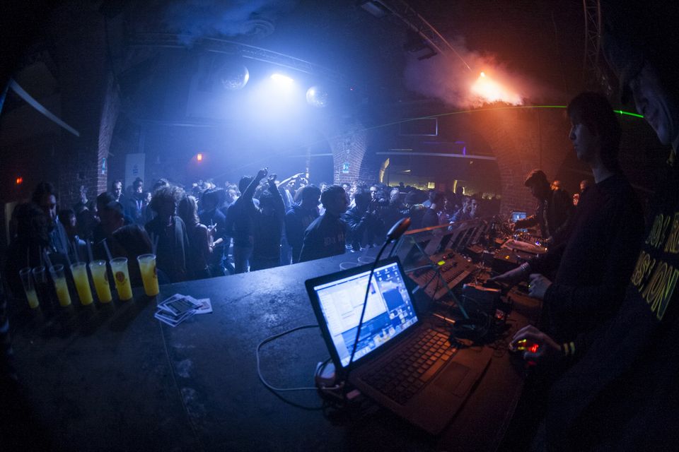 Laptop and mixer at the decks with a crowd under blue stage light