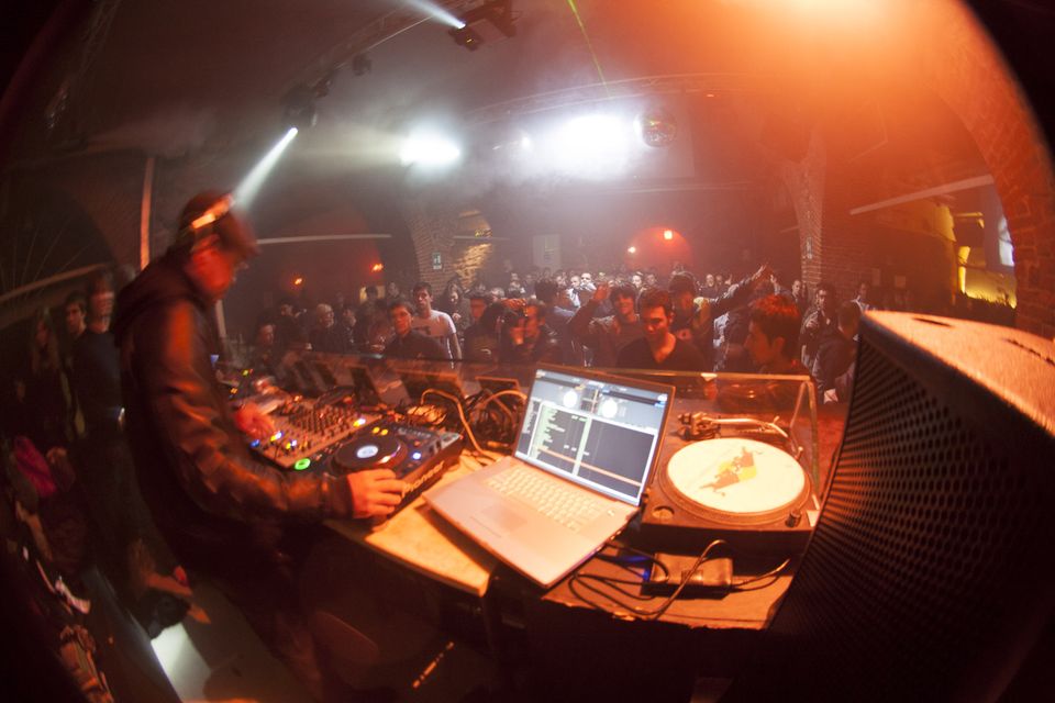 DJ at the decks with a laptop and a dancing crowd in hazy red light