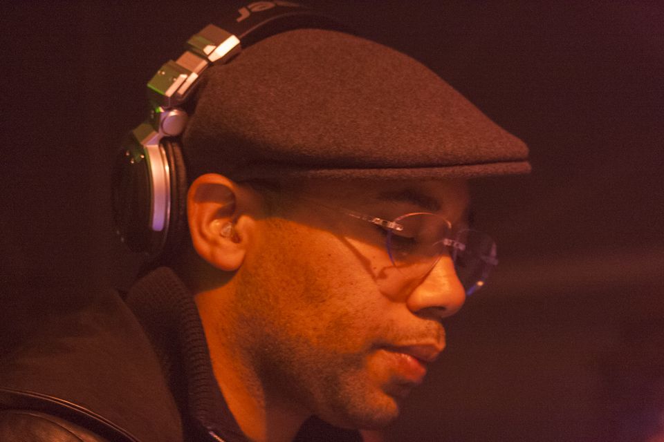 Close profile of a DJ in a flat cap, glasses and headphones in red light