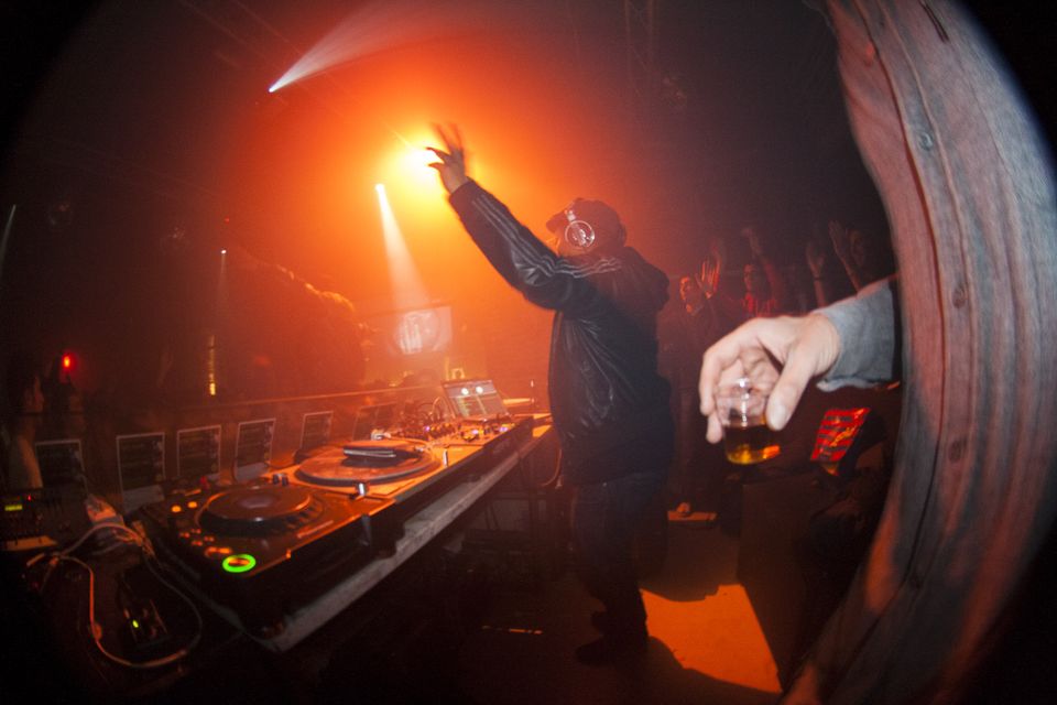 DJ raising an arm at the decks beneath a bright orange spotlight