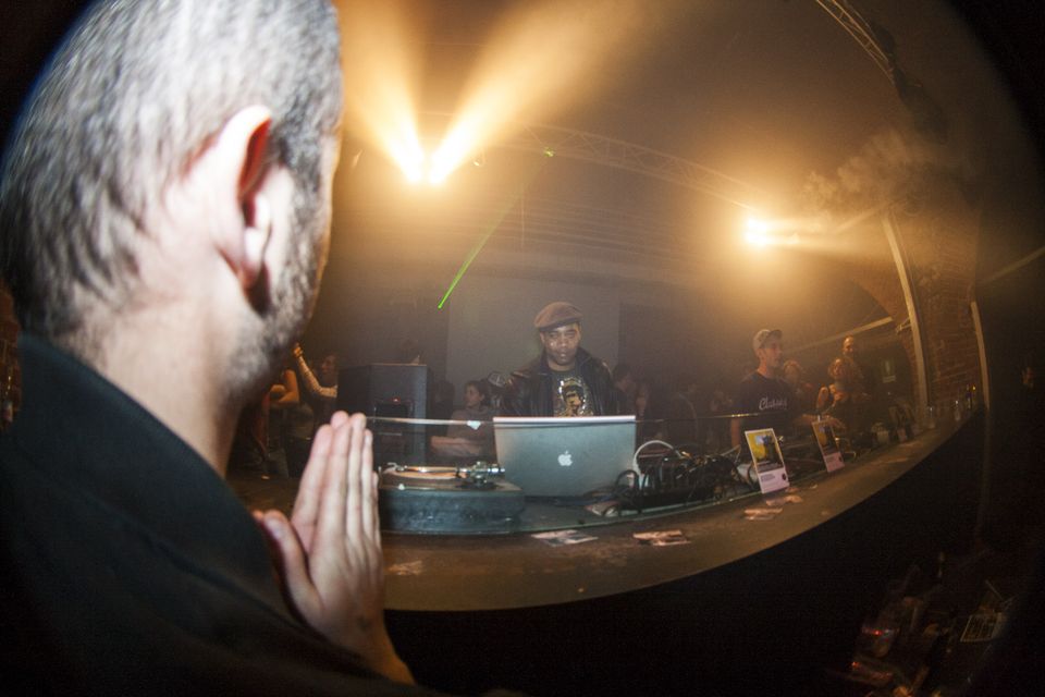 Man pressing his hands together before the booth, DJ with a laptop beyond