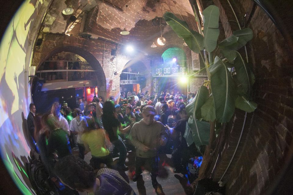 Crowd dancing under green and yellow light beneath brick arches