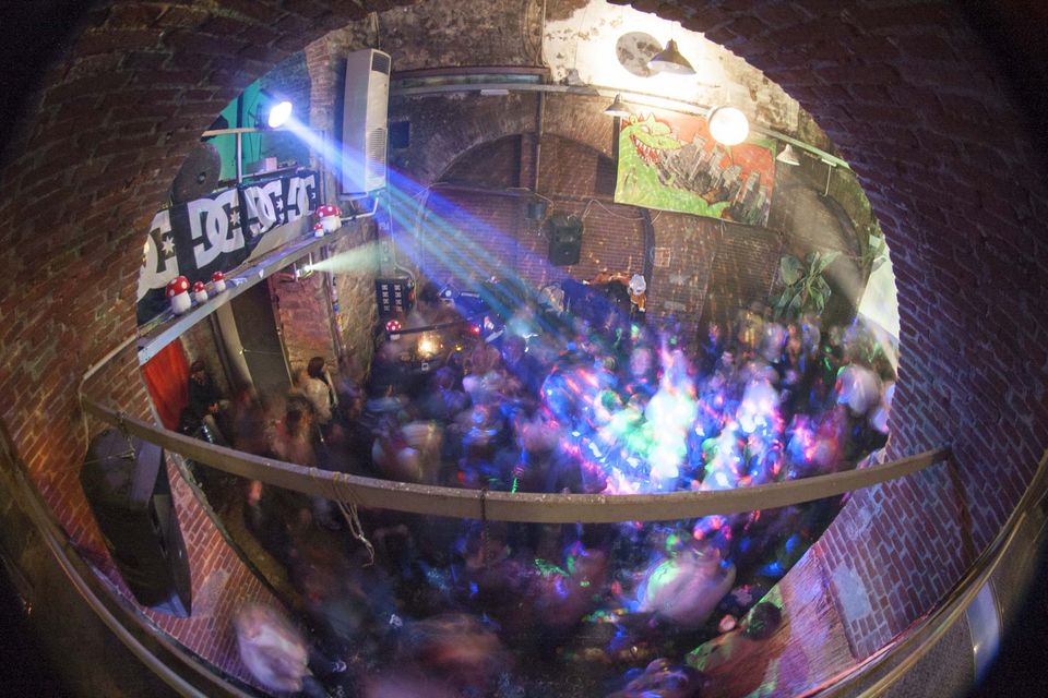 Fisheye view of dancers under beams of light in a brick cellar
