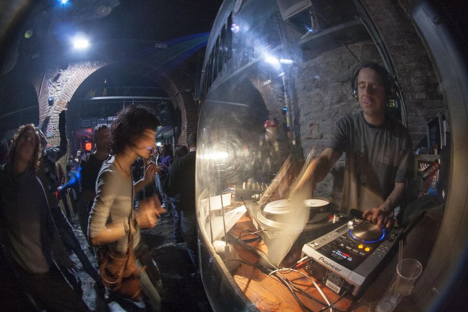 Dancer beside a DJ in a brick cellar club under blue light