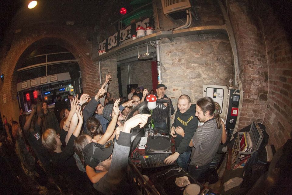 Hands raised toward the DJ booth in a stone and brick club