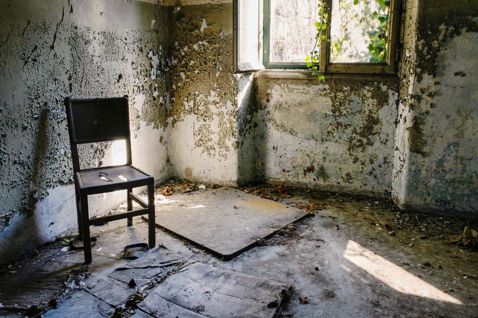Wooden chair in a corner of a room with peeling plaster