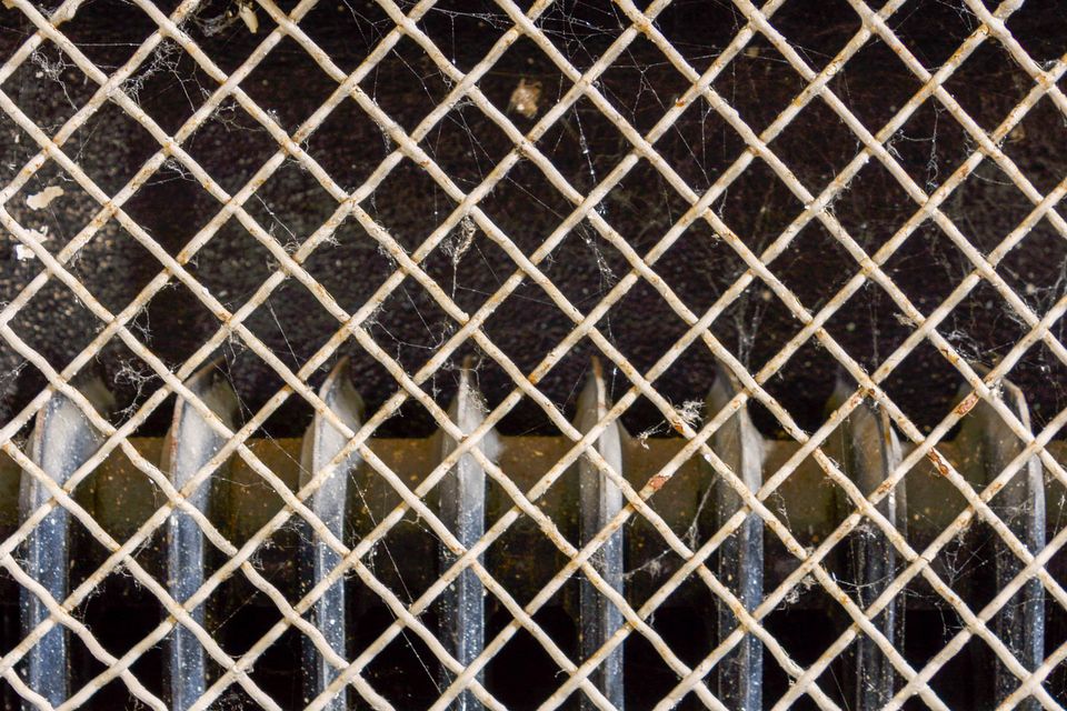 Rusty radiator behind a diamond wire mesh covered in cobwebs