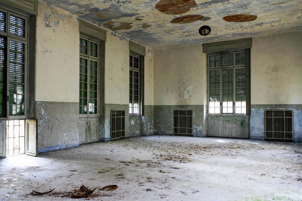 Large empty hall with tall shuttered windows and a stained ceiling