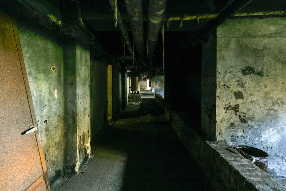 Dark basement corridor with pipes overhead and stained walls