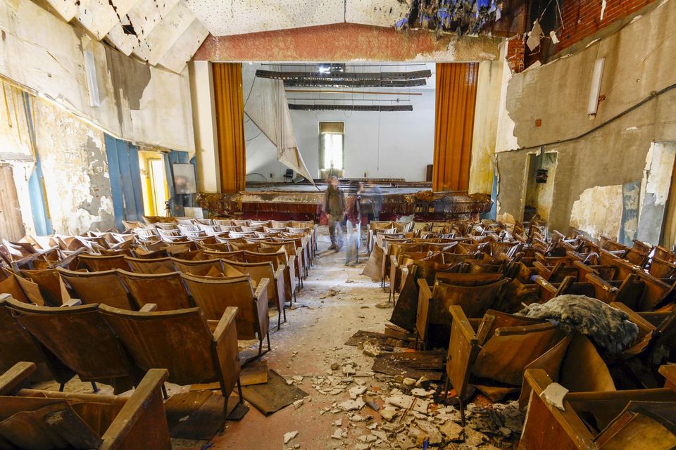 Theatre hall with rows of broken wooden seats and a stage