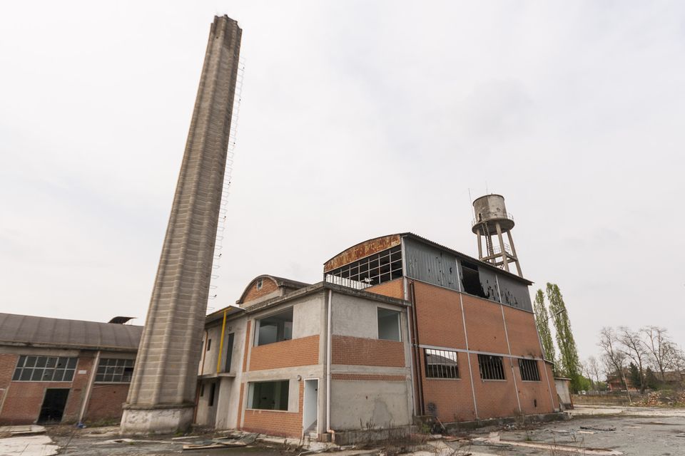 Tall concrete chimney, boiler house and water tower under grey sky