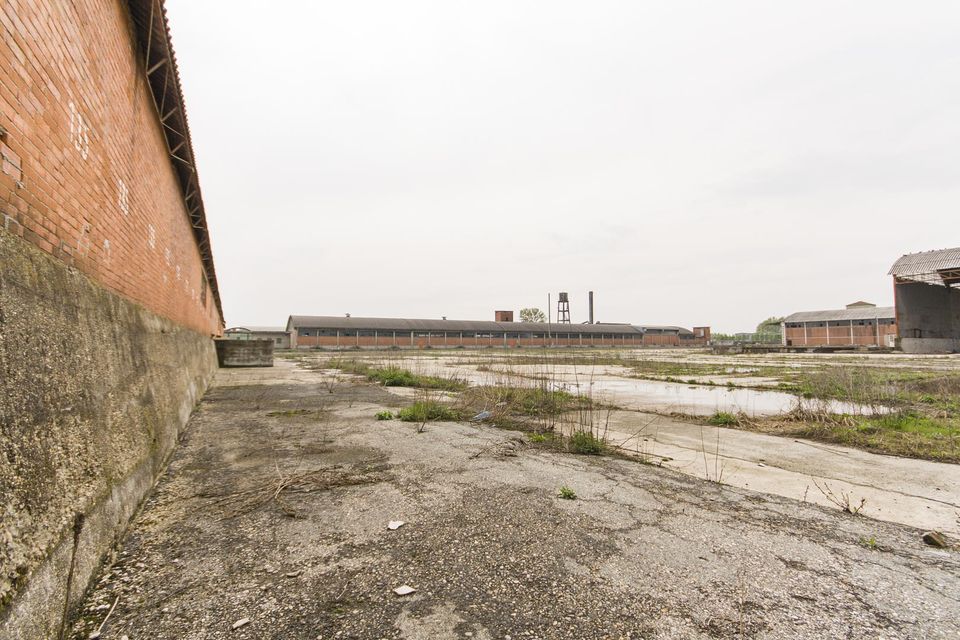 Wide empty yard with long brick sheds in the distance