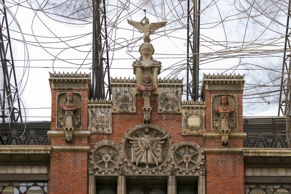 Brick facade topped by an eagle and carved busts behind wires