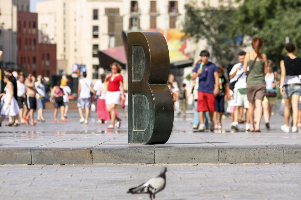 Bronze letter B sculpture with a pigeon and a crowd behind