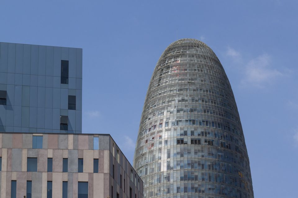 Rounded glass tower beside a grey block against blue sky