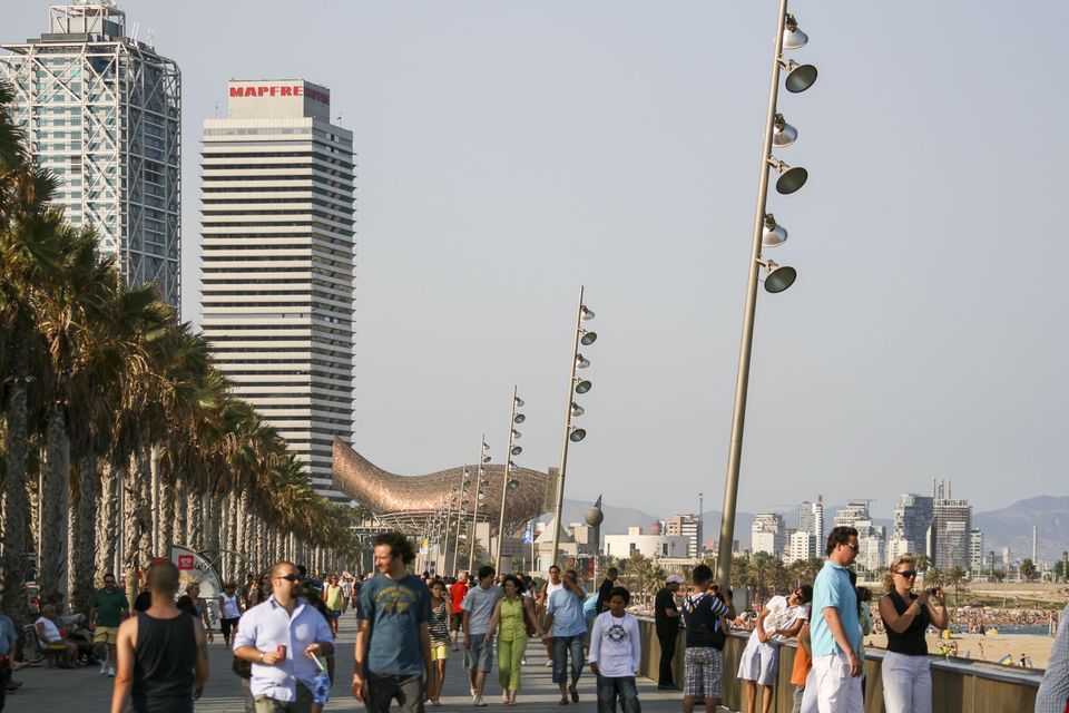 Seafront promenade with tall towers and a copper fish sculpture beyond