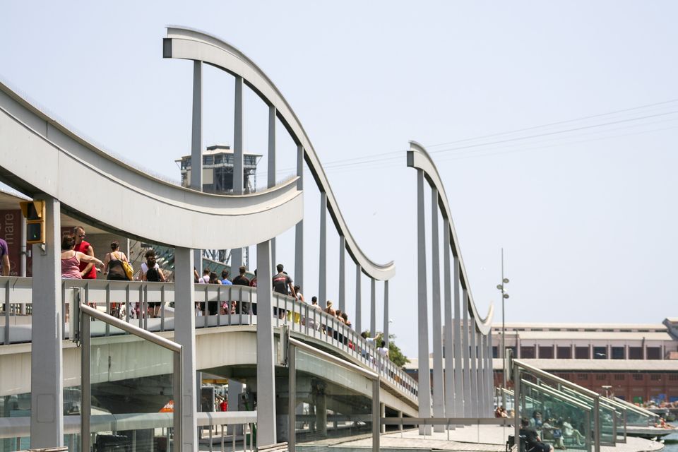 Curving white footbridge with people crossing the harbour